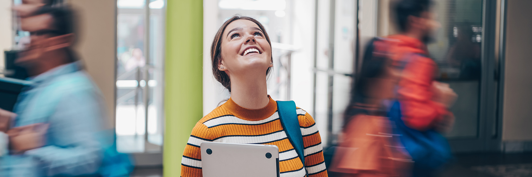 Female student holding a laptop and looking up